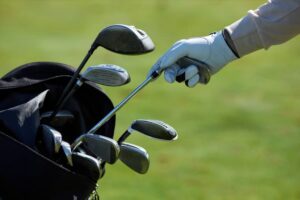 Closeup of golf player choosing club and taking out of golf bag against green grass