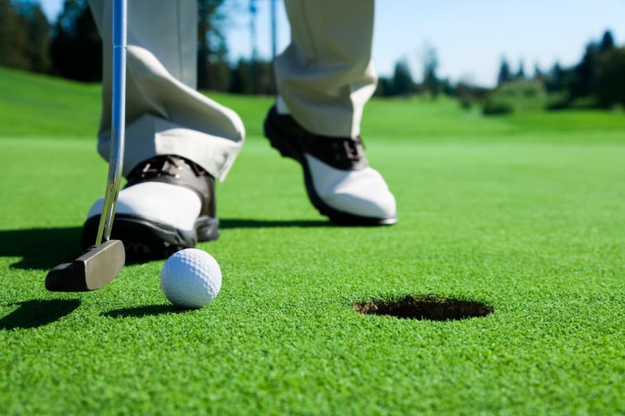 Golfer on putting green tapping ball into hole